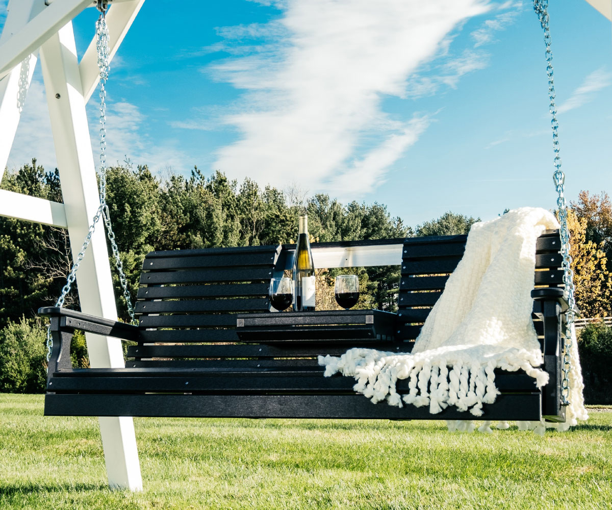 Outdoor swing with wine, glasses, and blanket on a sunny day.